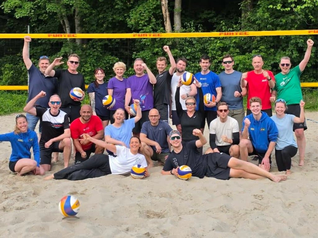 Gjengen samlet i sanden foran nettet etter beachvolleyball