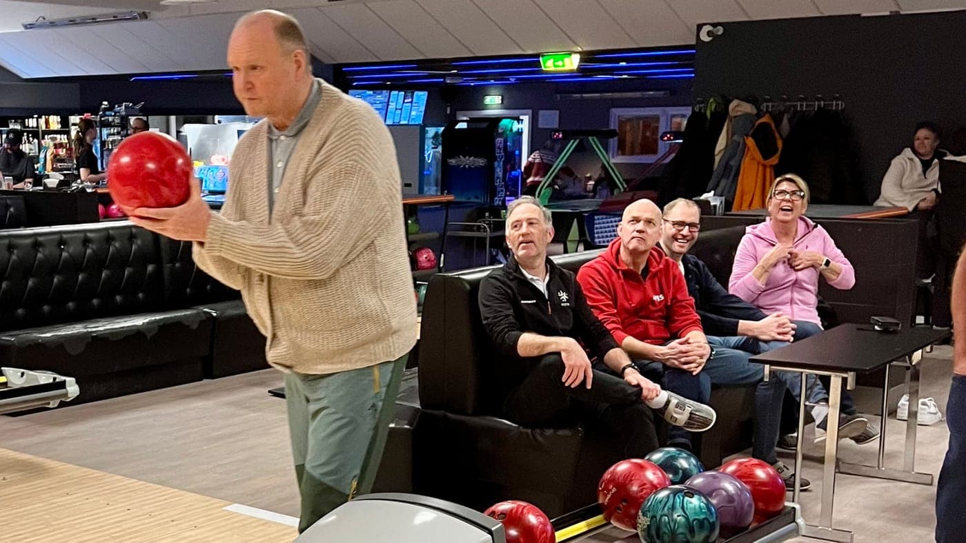 Medlem gjør seg klar med bowlingkula mens gjengen i sofaen ler